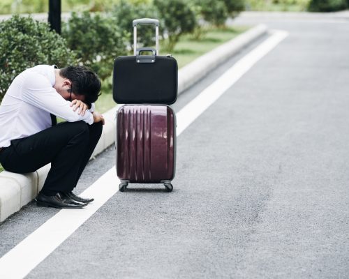 Tired or stressed businessman sitting on roadside with luggage next to him